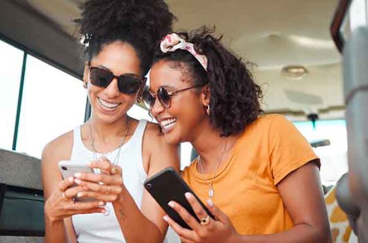 Black friends, phone and social media travel in communication together for road trip adventure. Happy and excited African American women sharing moments of traveling on mobile smartphone for vacation