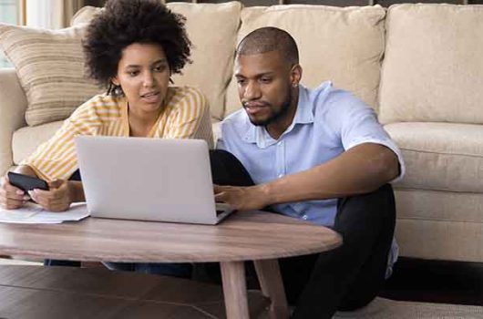 African couple sit in living room discuss receipts, control family budget, calculate household bills to pay, utility expenses, make payment via e-bank app on laptop, accounting, money control concept