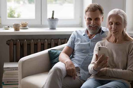 Mature couple sit on sofa staring at smart phone screen having video call remote conversation with grown up children or relative living abroad. Older gen use modern tech, virtual meeting event concept