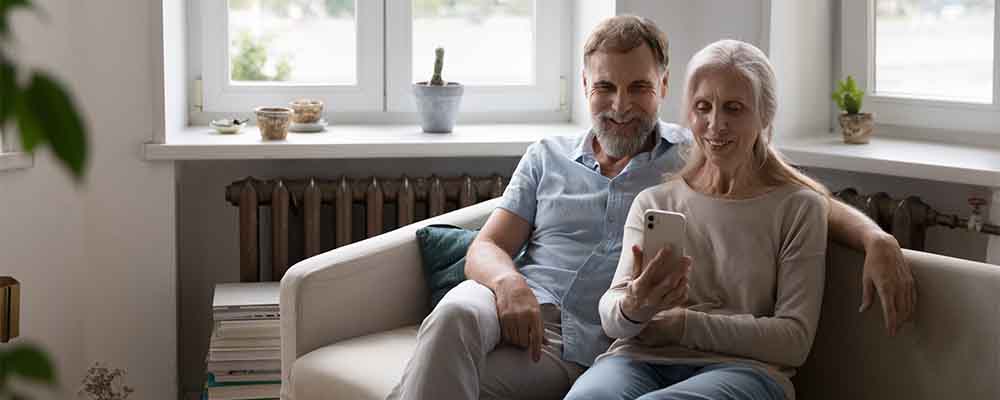 Mature couple sit on sofa staring at smart phone screen having video call remote conversation with grown up children or relative living abroad. Older gen use modern tech, virtual meeting event concept