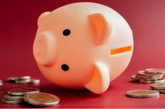 The empty pink piggy bank fall down around with little pile of less money coins on red background. Inflation, low cost, crisis economic, personal saving rate, low savings ratio concepts.