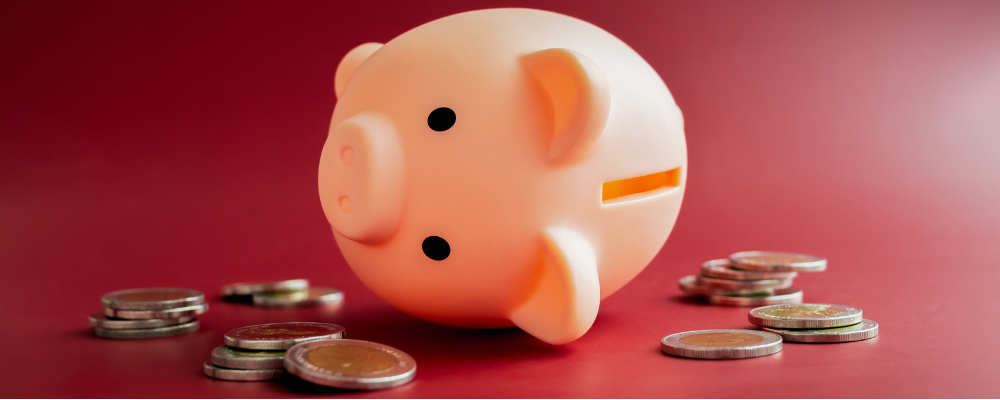 The empty pink piggy bank fall down around with little pile of less money coins on red background. Inflation, low cost, crisis economic, personal saving rate, low savings ratio concepts.